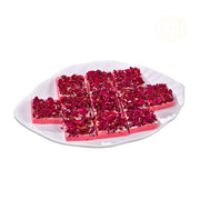 A plate of Gulkand Biscuit, which are pink colored biscuits garnished with rose petals, placed on a white plate.
